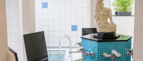 Un baño moderno con un lavabo de azulejos azules, una estatua blanca y un reloj verde en la pared.