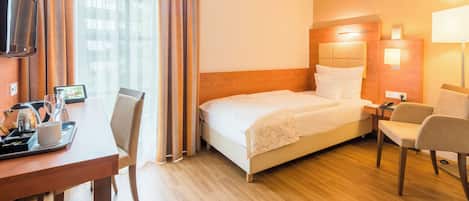 A hotel room with a bed, bedside table, chair, desk, and a television.