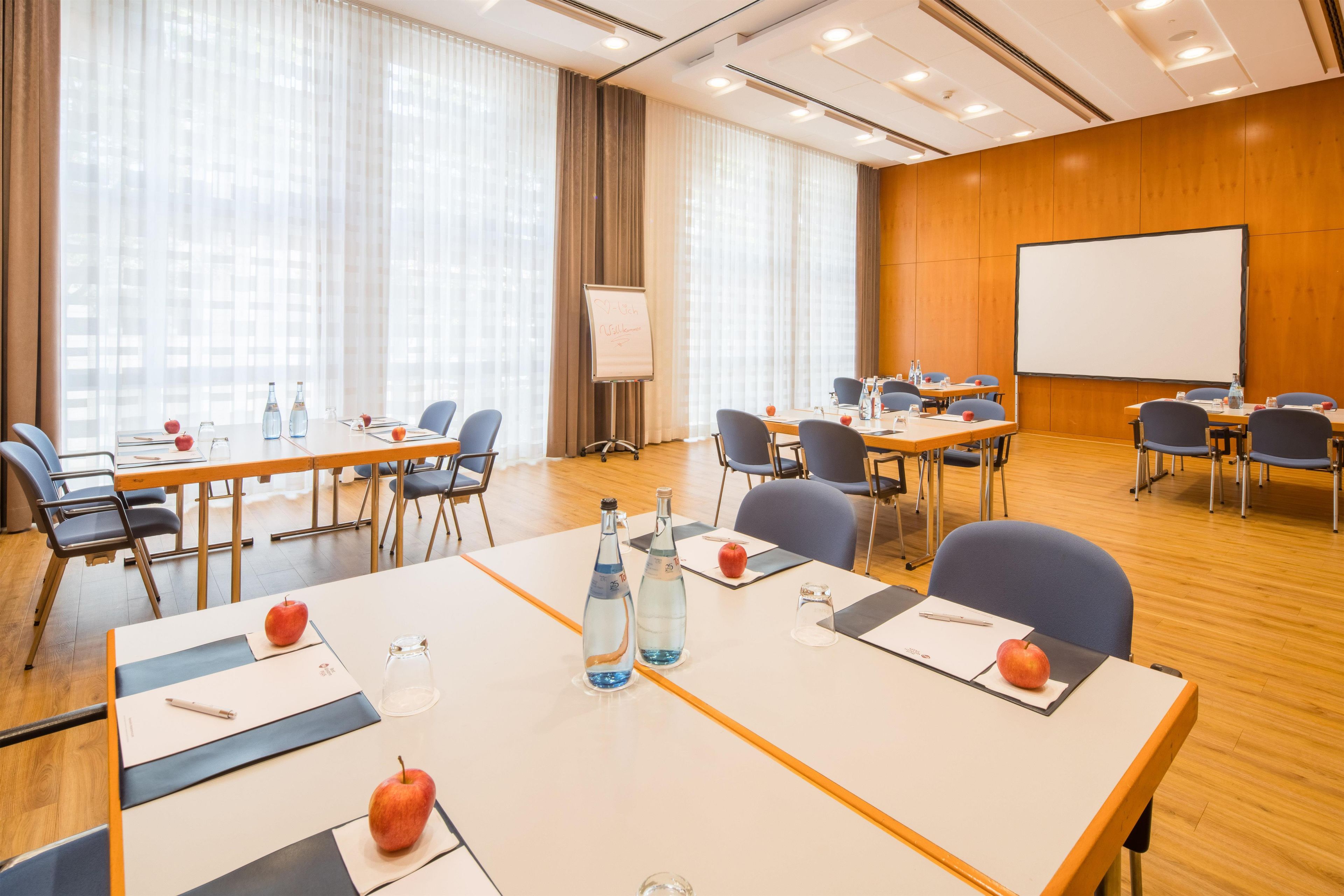 A conference room with tables, chairs, a whiteboard, and a projector screen.