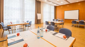 A conference room with tables, chairs, a whiteboard, and a projector screen.