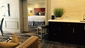 Ein Hotelzimmer mit Bett, einer kleinen Küchenzeile, einer Sitzecke mit einer Bank und einer Tür zu einem weiteren Raum.