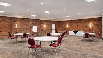 A conference room with brick walls, white tables, and red chairs.