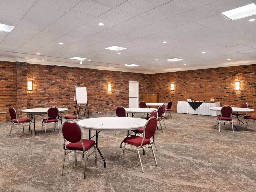 A conference room with brick walls, white tables, and red chairs.