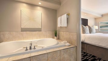 Un baño moderno con una bañera grande, un toallero en la pared y, en la habitación contigua, una cama con una colcha estampada.