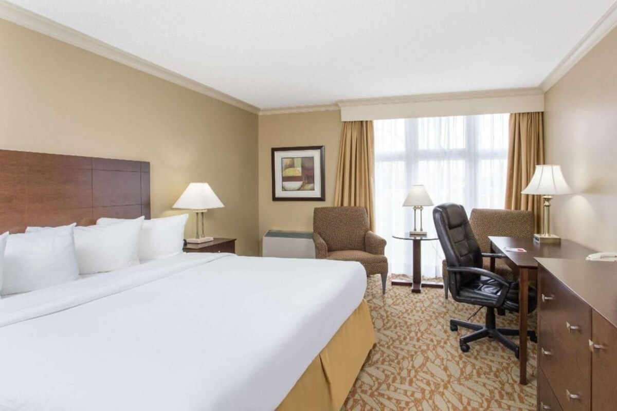 A hotel room with a large bed, two chairs, a desk, and a lamp.