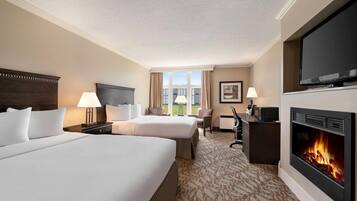 A hotel room with two beds, a television, a fireplace, and a desk with a lamp.