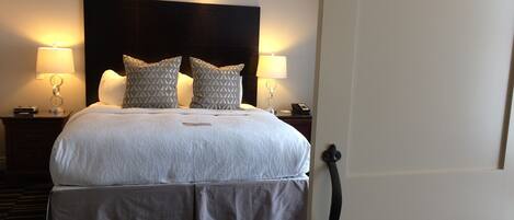 A hotel room with a large bed, two bedside lamps, a headboard, a bedside table with a phone, and a patterned carpet.