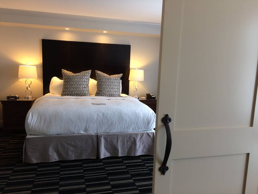 A hotel room with a large bed, two bedside lamps, a headboard, a bedside table with a phone, and a patterned carpet.