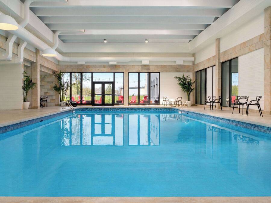 An indoor swimming pool with clear glass walls, a tiled floor, and ceiling lights.