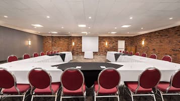 A conference room with a long table, red chairs, and a projector screen.
