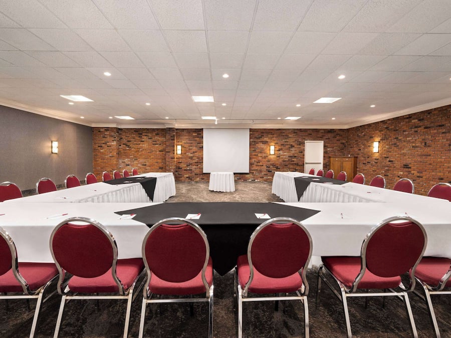 A conference room with a long table, red chairs, and a projector screen.