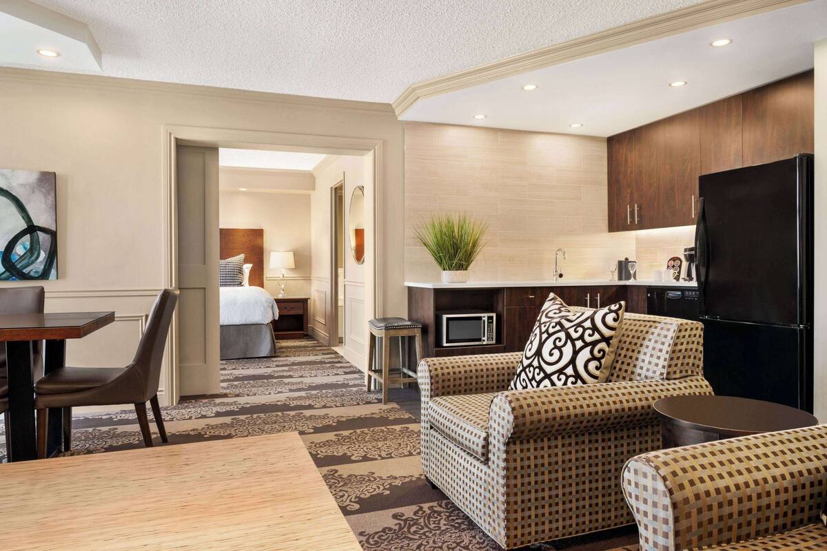 Habitación de hotel con comedor, sofá, una mesita, microondas, refrigerador y una planta.