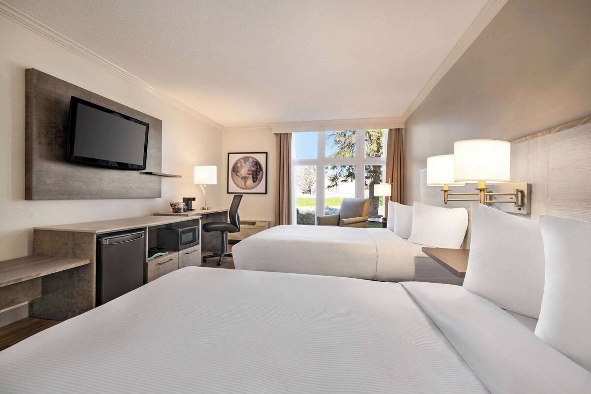 Habitación de hotel con una cama grande, un escritorio con televisor, una silla y una ventana con vistas al exterior.