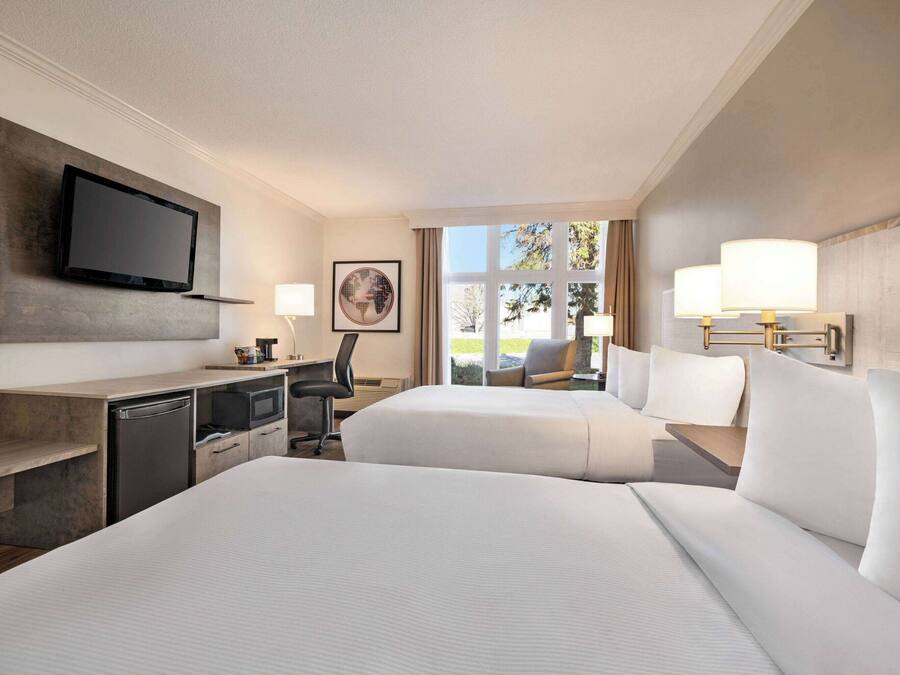 Habitación de hotel con una cama grande, un escritorio con televisor, una silla y una ventana con vistas al exterior.