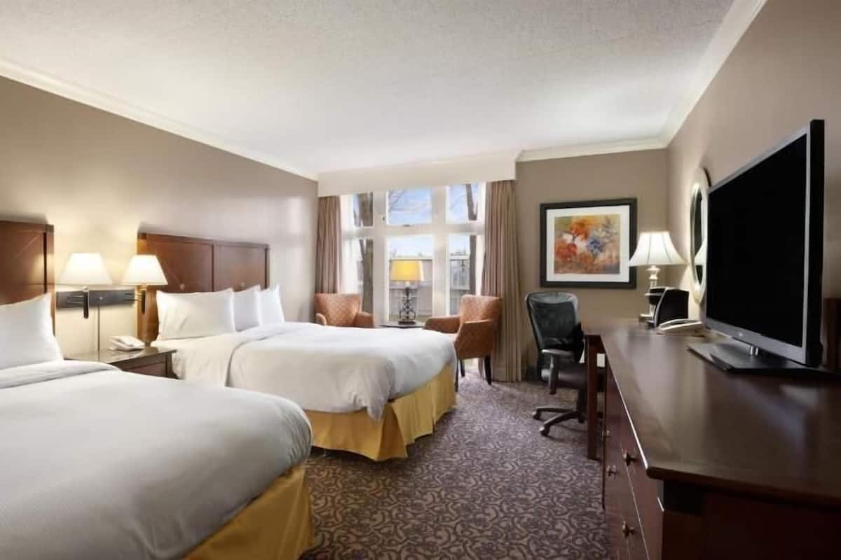 A hotel room with two beds, a desk, a TV, and a window with curtains.