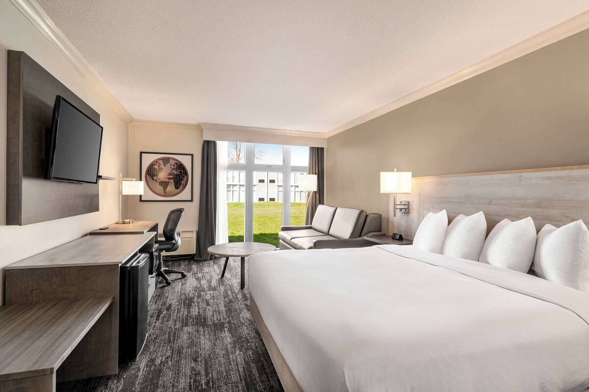 Una habitación de hotel con una cama grande, un escritorio con silla, televisión y vistas al exterior.