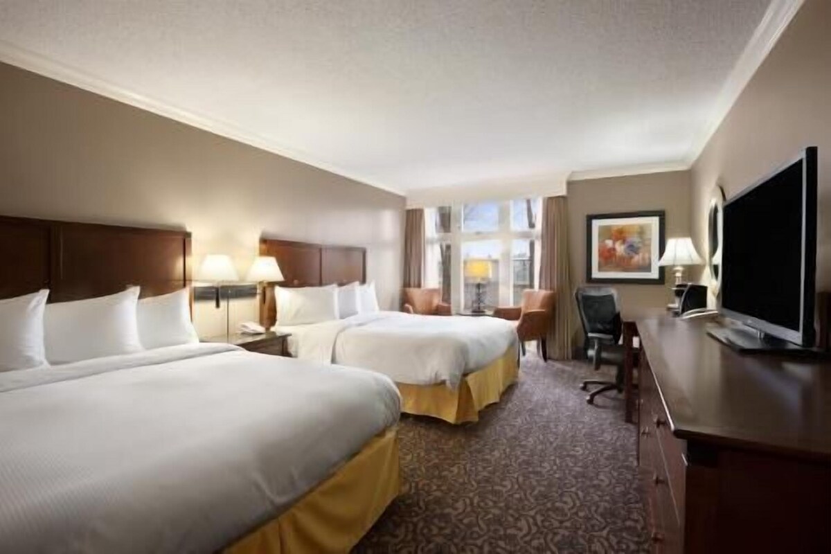 A hotel room with two beds, a desk, a TV, and a window.