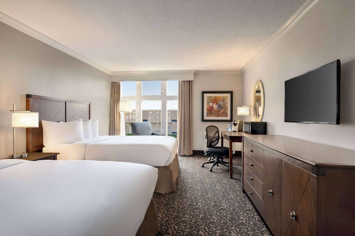 Habitación de hotel con dos camas, un escritorio, una silla, un televisor y una ventana con cortinas.