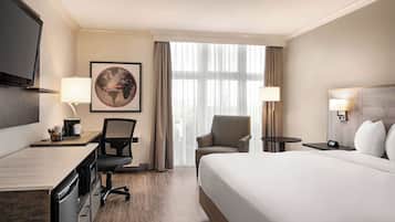 A hotel room with a large bed, a desk with a chair, a television, and a large window with curtains.