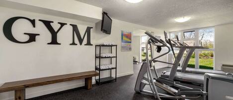 A gym with a treadmill, a bench, and a wall-mounted shelf with towels.