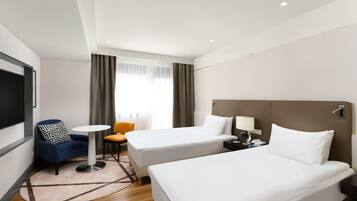 Een hotelkamer met twee eenpersoonsbedden, een klein rond tafeltje, een blauwe fauteuil, een stoel en een televisie.