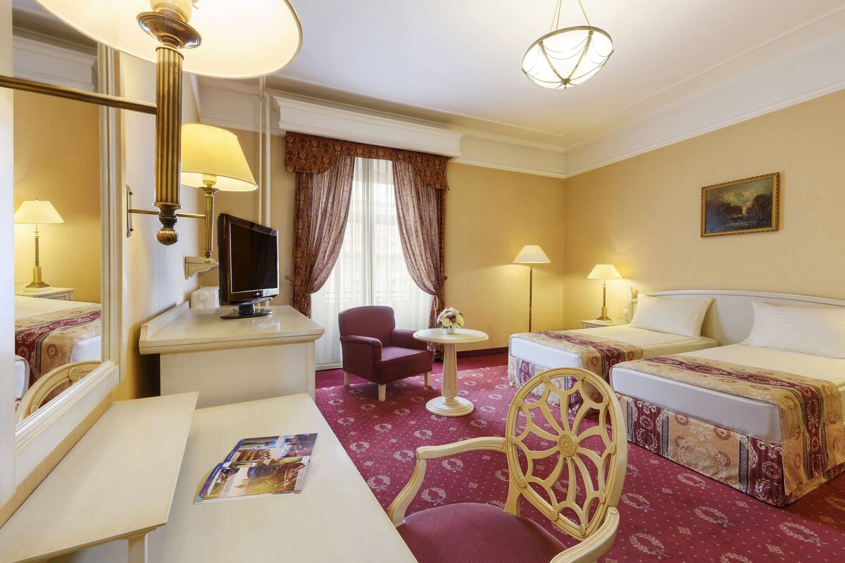 Een hotelkamer met een bed, twee nachtkastjes, een bureau, een stoel, een televisie en een raam met gordijnen.