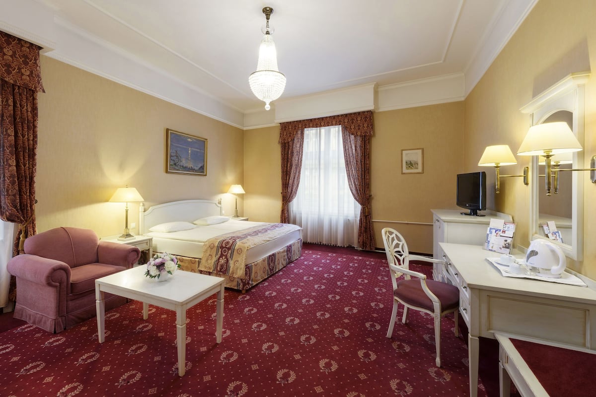Een hotelkamer met een bed, twee nachtkastjes met lampen, een bureau met een stoel, een televisie en een groot raam met gordijnen.