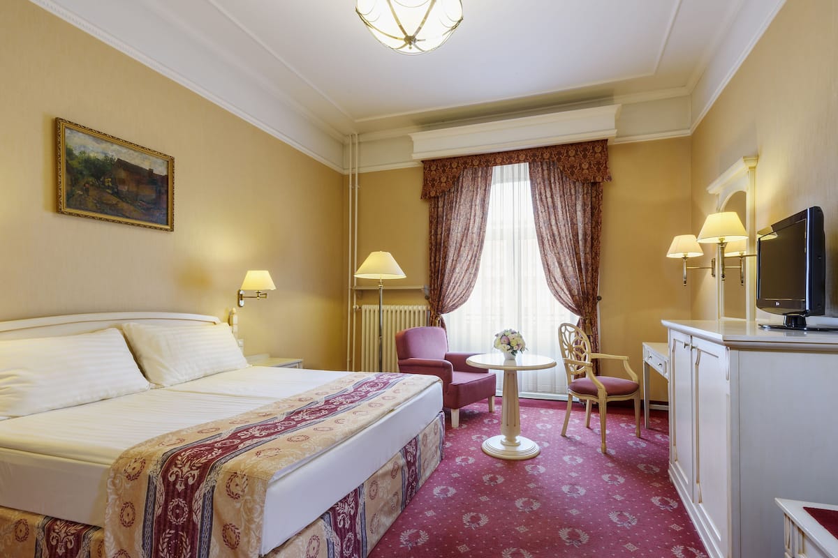 Een hotelkamer met een bed, een bureau, twee stoelen, een tafeltje met een vaas en een televisie.