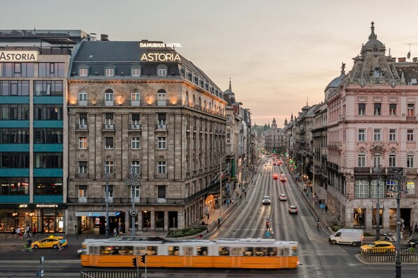 A historic building with the sign "Danubius Hotel Astoria" and a tram in the foreground.