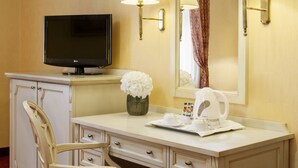 A hotel room with a TV, a desk with a lamp, a mirror, a chair, and a vase with flowers. - Danubius Hotel Astoria City Center (Budapest)