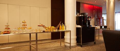A buffet setup with various food items and beverages, a coffee machine, and a seating area.