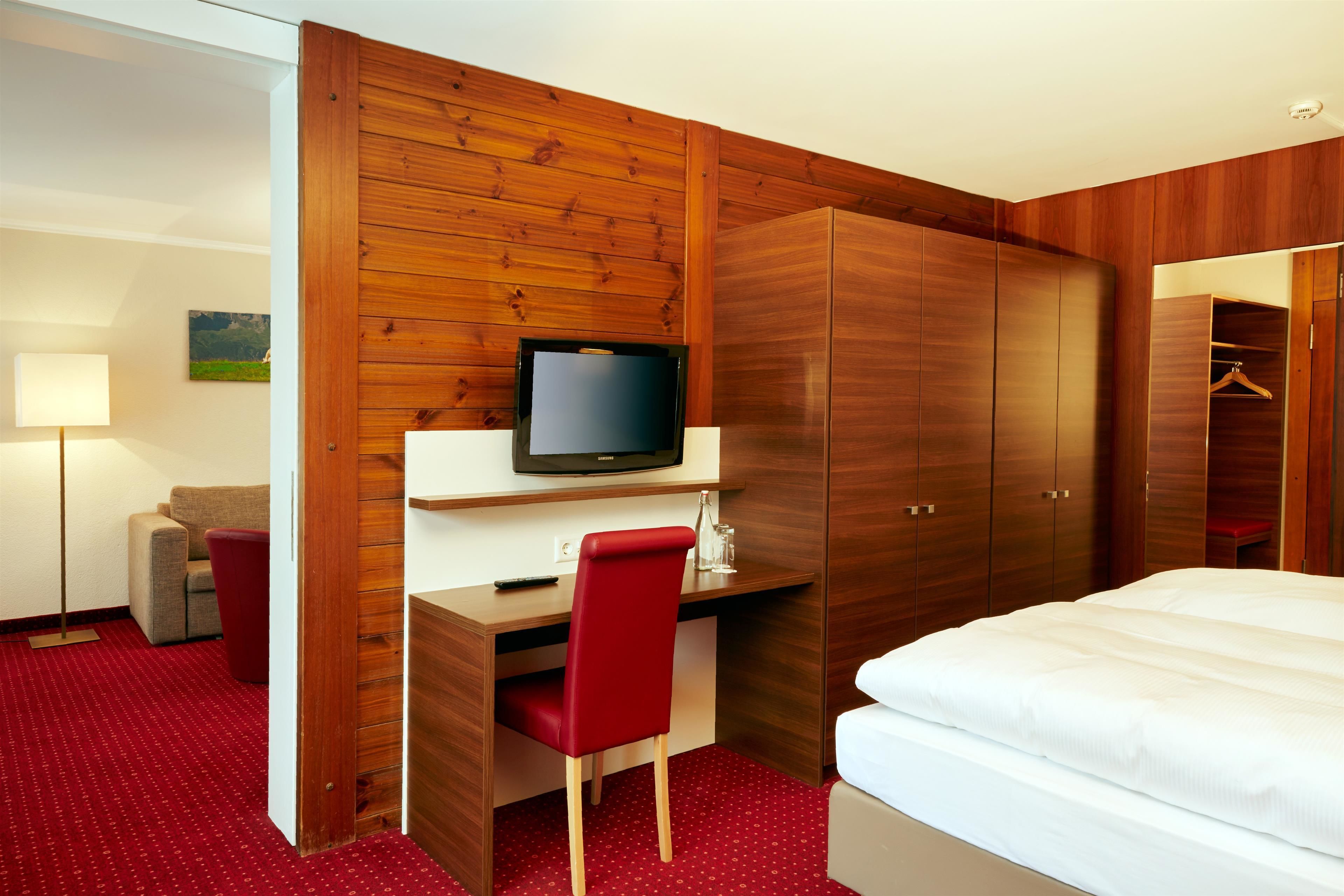 Une chambre d’hôtel avec une armoire en bois, un bureau avec une chaise, une télévision et un lit.