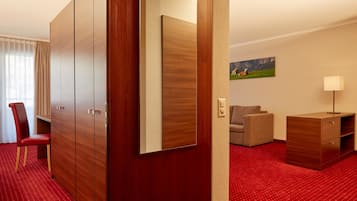 Habitación de hotel con alfombra roja, armario de madera, un escritorio, una silla, un sofá, una lámpara y un cuadro en la pared.