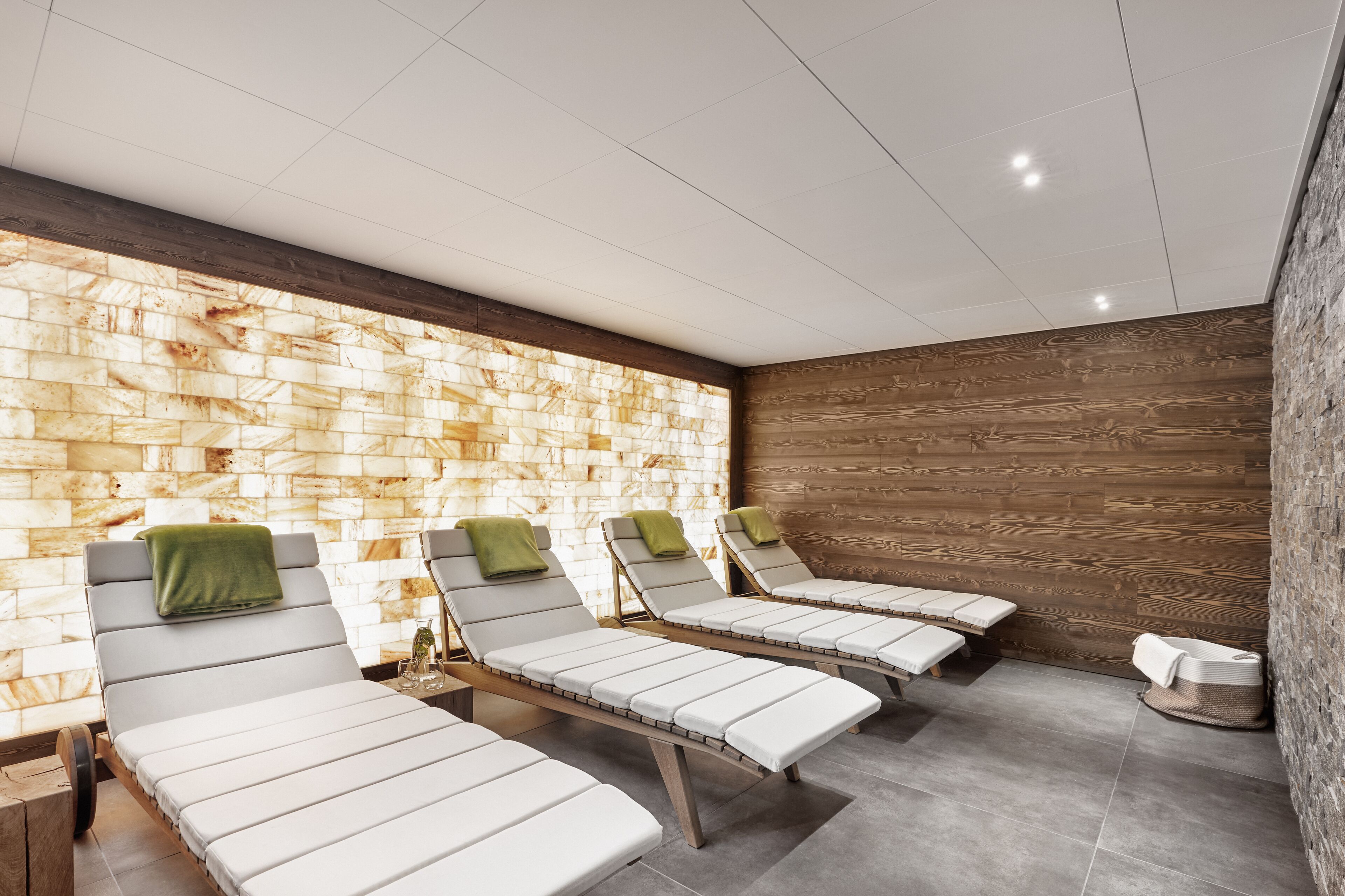 Un área de spa con tres tumbonas, una pared de piedra, paneles de madera y suelo de baldosas.