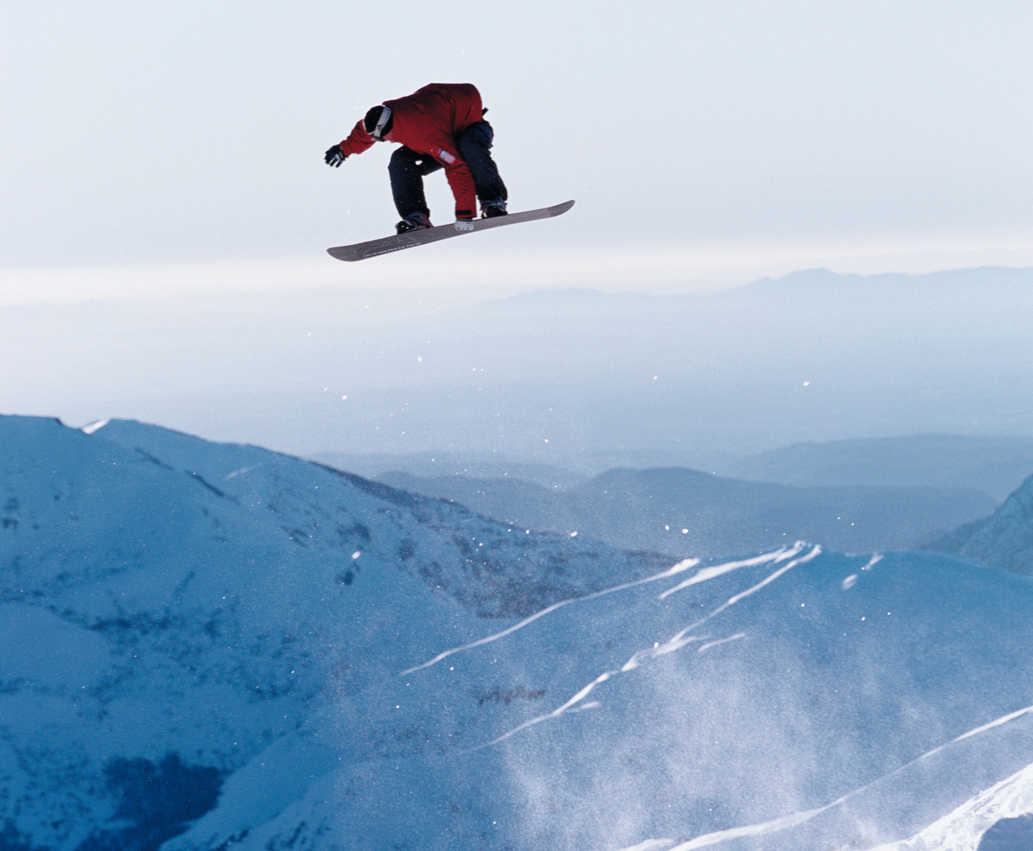 A snowboarder in mid-air above a snowy mountain landscape.