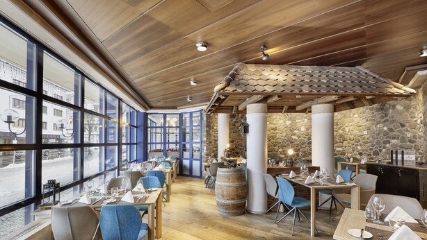 A restaurant with large windows, wooden ceiling, stone walls, and blue chairs. - Hotel Regina Titlis, a Trademark Collection by Wyndham (Engelberg)
