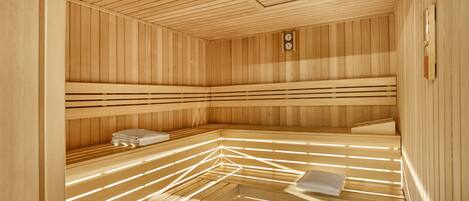 A sauna with wooden slats and benches, a clock, and a towel rack.