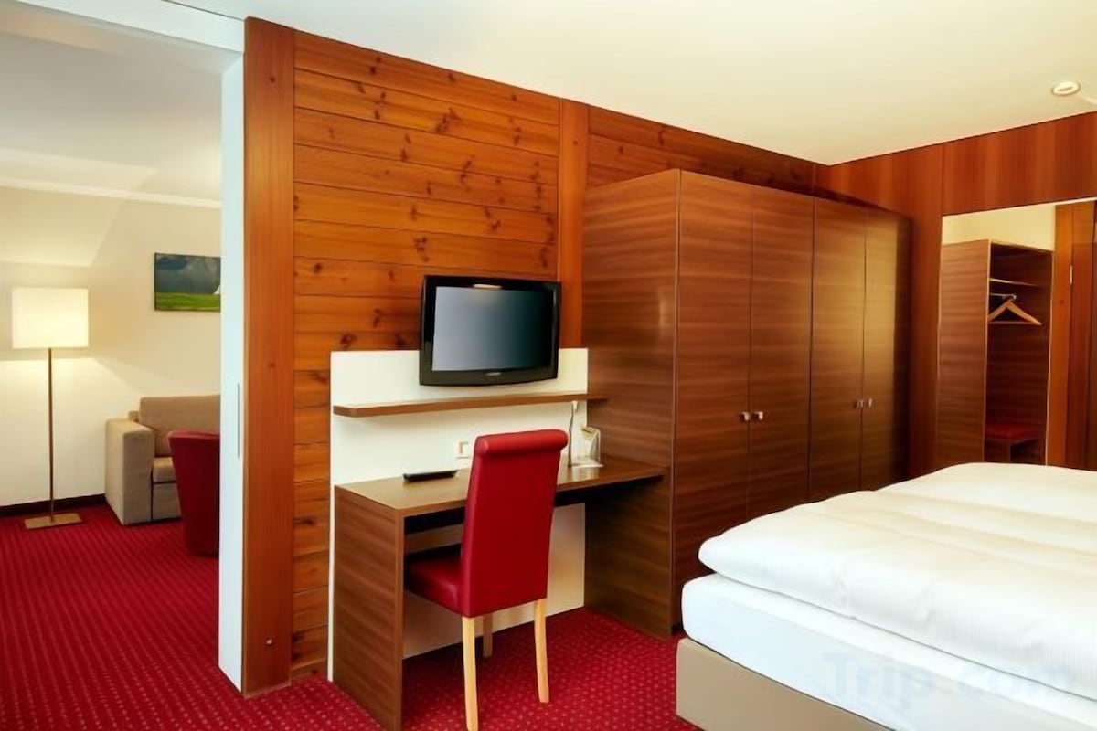 A hotel room with a bed, a desk with a chair, a television, and a wardrobe.