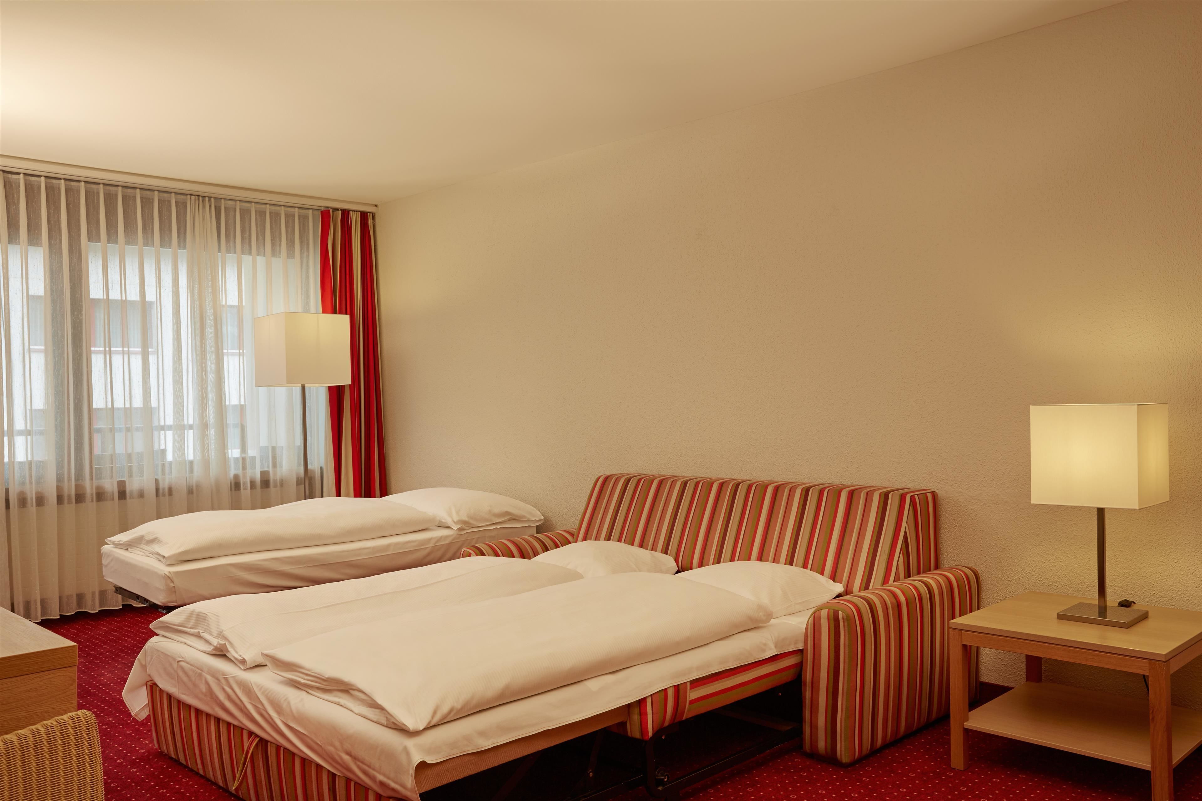 Une chambre d’hôtel avec deux lits, un canapé, un bureau et deux lampes.