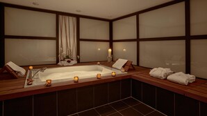A large, rectangular bathtub with a wooden frame, surrounded by dark tiles. There are three lit candles on the edge of the tub, and a wooden bench with towels on it. - Hotel Regina Titlis, a Trademark Collection by Wyndham (Engelberg)