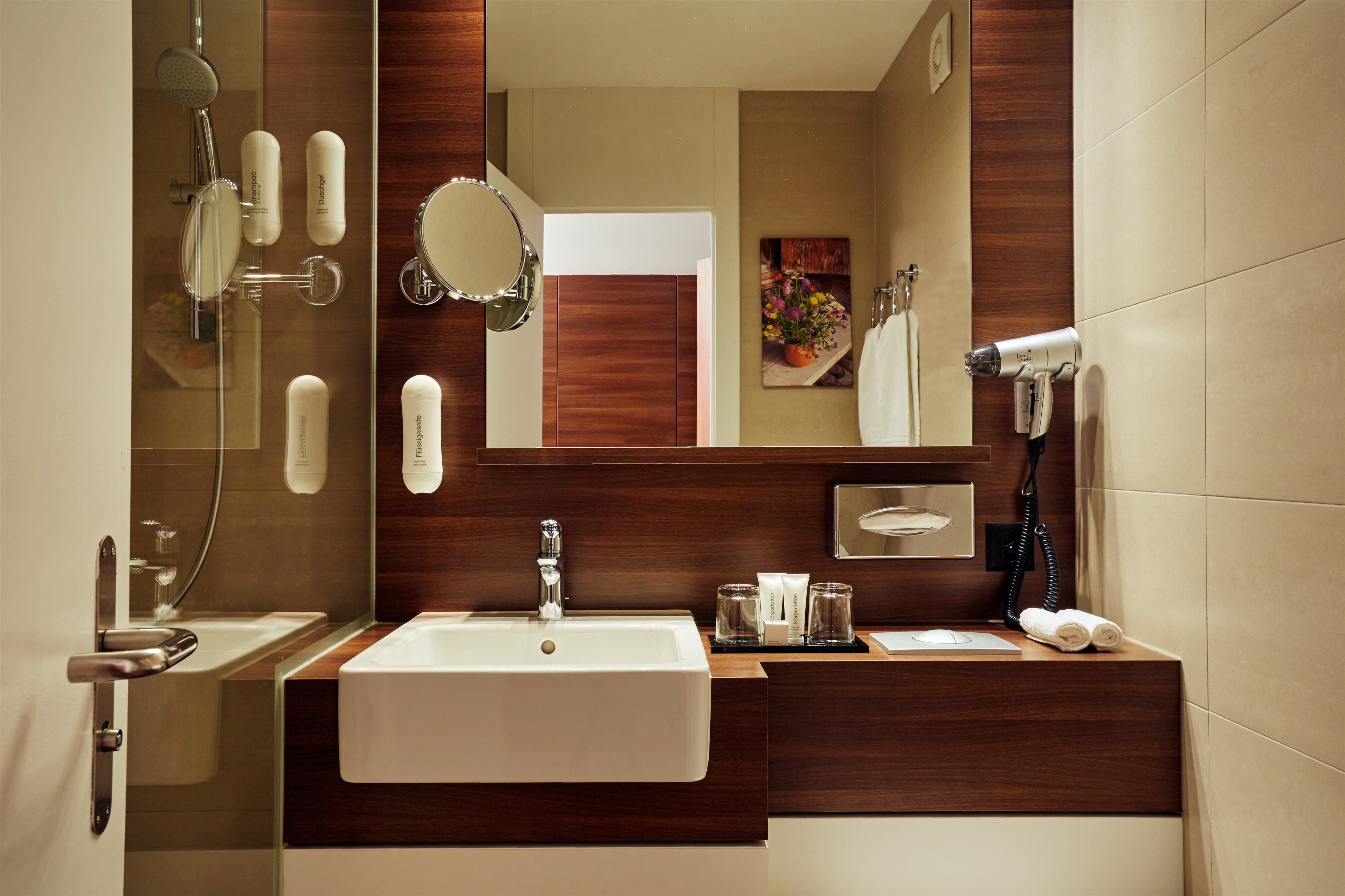 A modern bathroom with a large mirror, a sink, a shower, and a hairdryer.