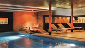 A modern indoor pool area with a stone wall, wooden ceiling, and lounge chairs. - Hotel Regina Titlis, a Trademark Collection by Wyndham (Engelberg)