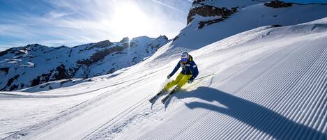 A skier on a snowy slope with a clear sky and mountains in the background.
