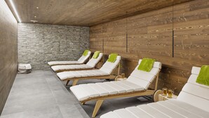 A spa room with wooden panel walls, stone walls, and white cushioned chairs with green towels. - Hotel Regina Titlis, a Trademark Collection by Wyndham (Engelberg)