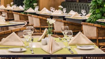 Une salle de restaurant avec des tables dressées pour le service, agrémentée de sets de table verts, de serviettes pliées et de verres transparents.