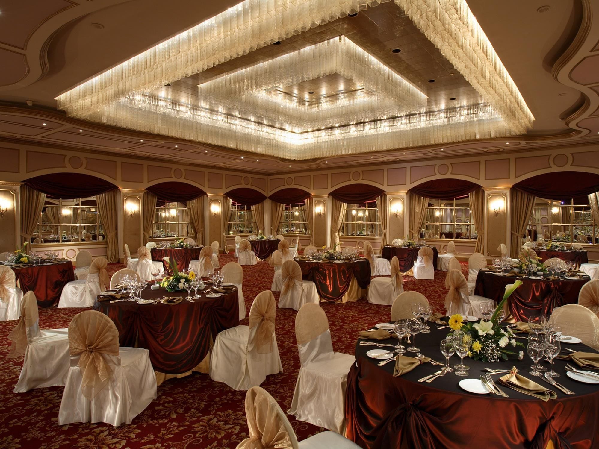 Een feestzaal met ronde tafels, stoelen en kroonluchters.