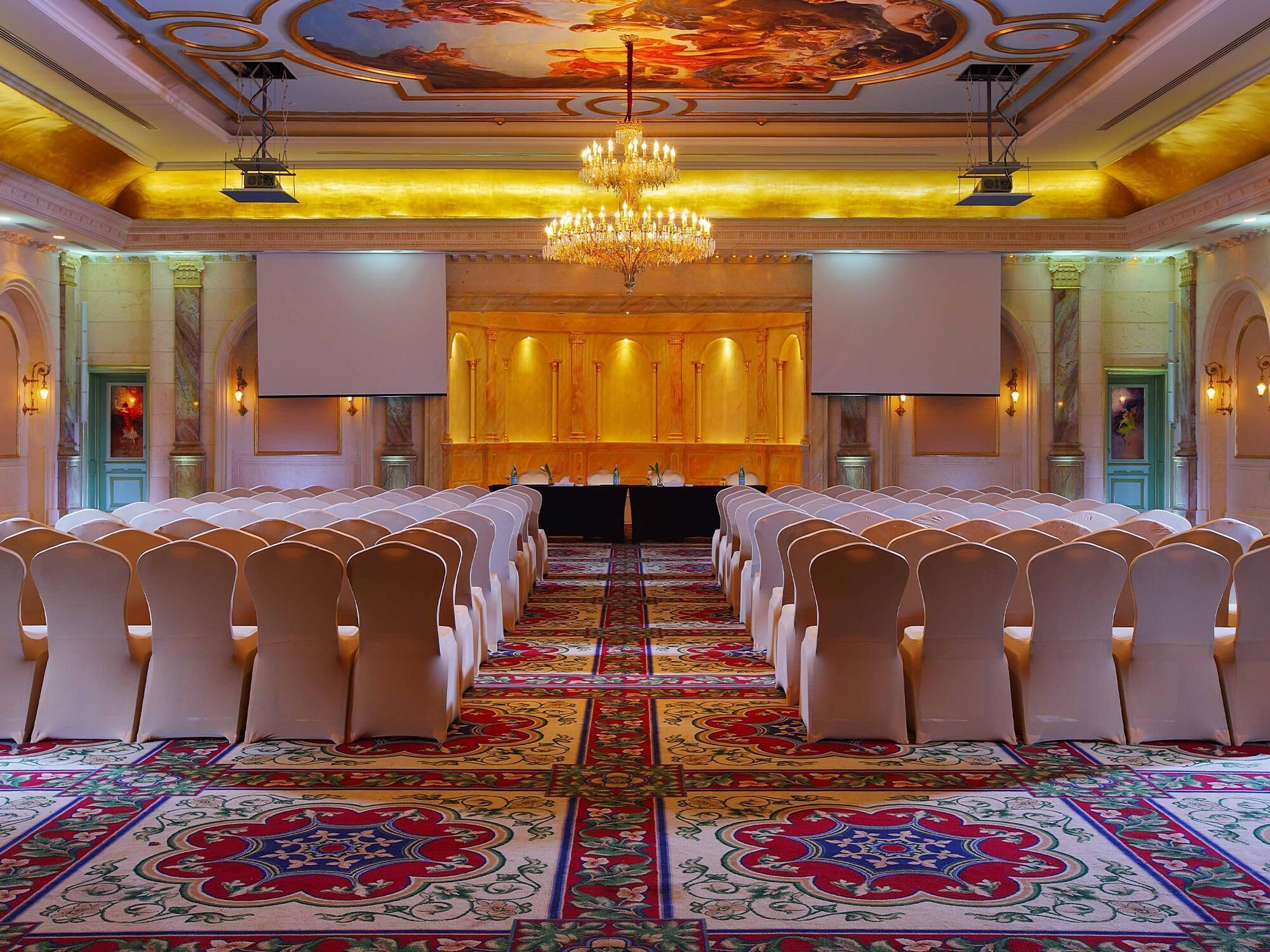 A formal event space with rows of chairs, a large chandelier, and a carpeted floor.