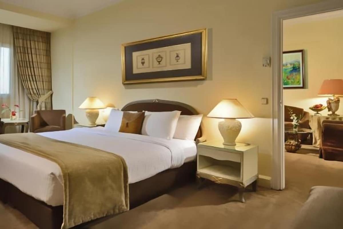Una habitación de hotel con una cama grande, dos mesitas de noche con lámparas, una silla y un escritorio con lámpara.