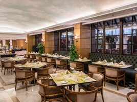 Un'area ristorazione di un hotel con diversi tavoli apparecchiati per gli ospiti, con sedie in vimini e una panca imbottita verde.
