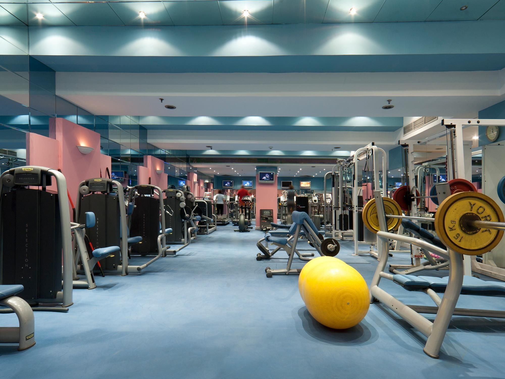 Ein Fitnessraum mit verschiedenen Trainingsgeräten, darunter Kraftgeräte und Kurzhanteln, sowie eine große Trainingskugel.